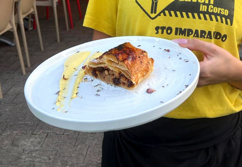 Cameriere sorregge un piatto con strudel di mele